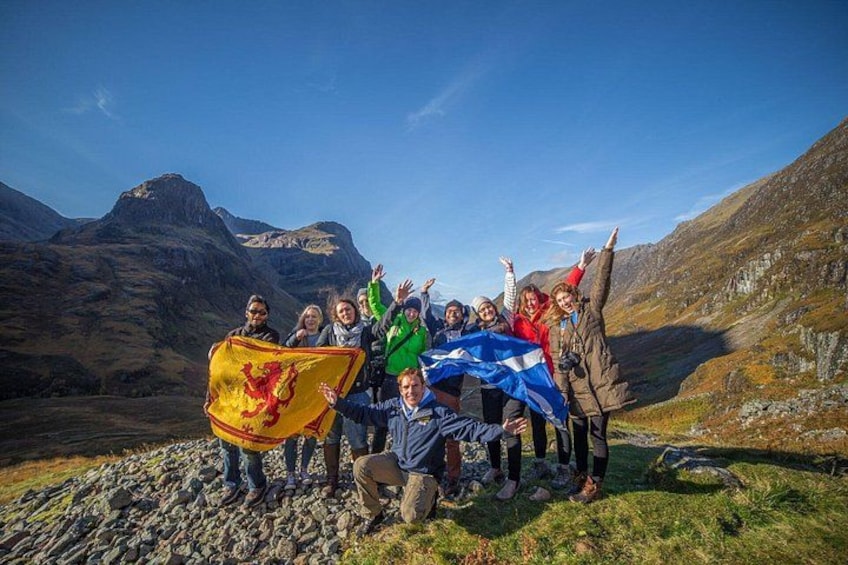 A group of people on a mountain with flags, rocky terrain, and a clear sky. 4
