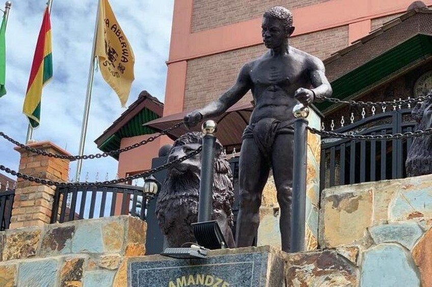 A statue of a muscular man holding a sword, with a lion at his feet. The statue is mounted on a stone pedestal with the name 'AMAND' visible. 4