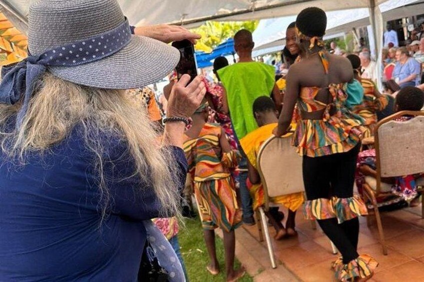 A person taking a photo, people in colorful traditional attire, and a tent. 1