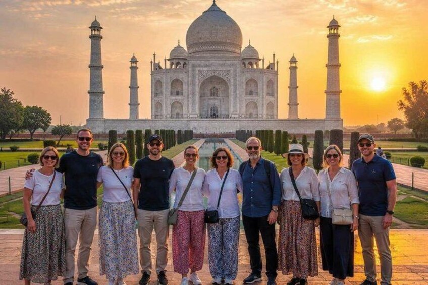 Eine Gruppe von Menschen steht vor dem Taj Mahal, während die Sonne im Hintergrund untergeht. 1