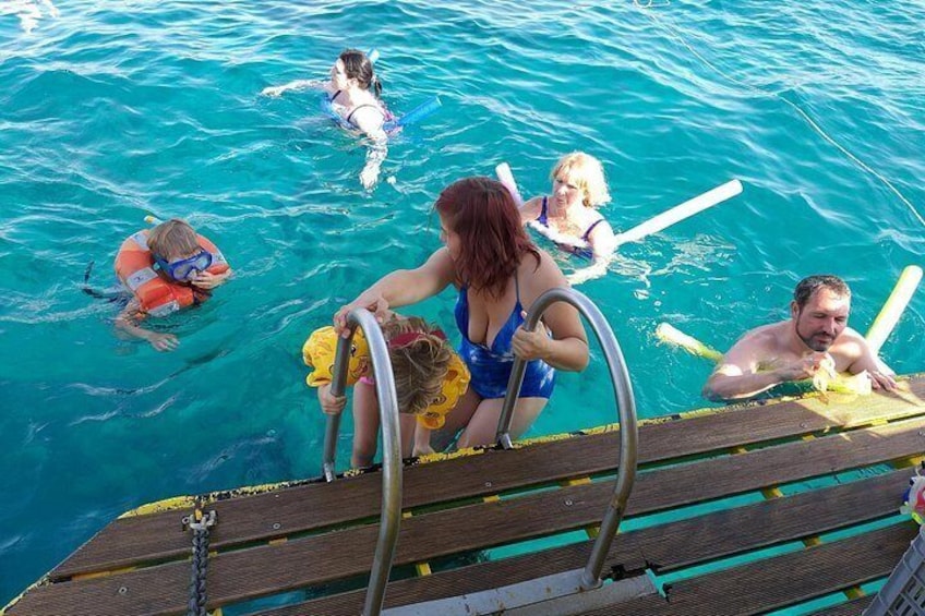 People swimming in a clear blue pool with a wooden deck in the foreground. 2