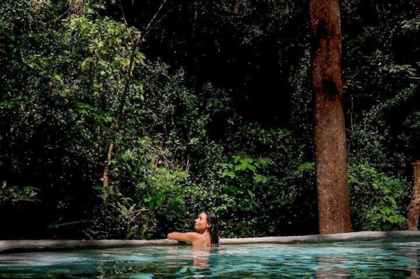 A person relaxing in a pool surrounded by dense forest. 2