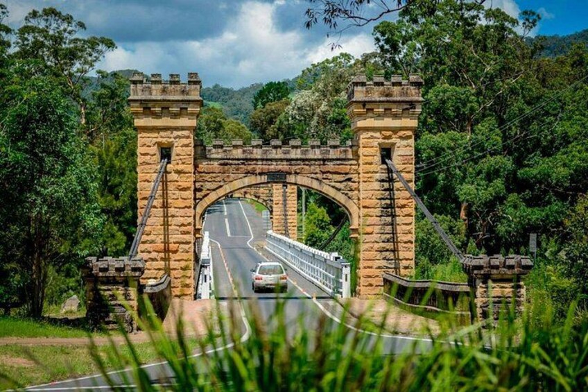 A stone bridge with a guardhouse, a road passing underneath, and lush greenery around. 5