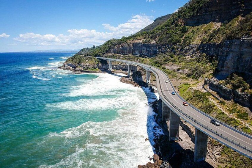 A coastal highway with a bridge spanning the water, cliffs, and a clear sky. 4