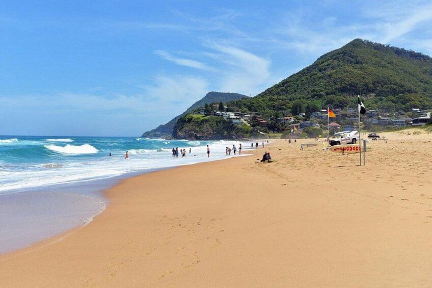 A beach with people, a flag, and a mountain in the background. 3