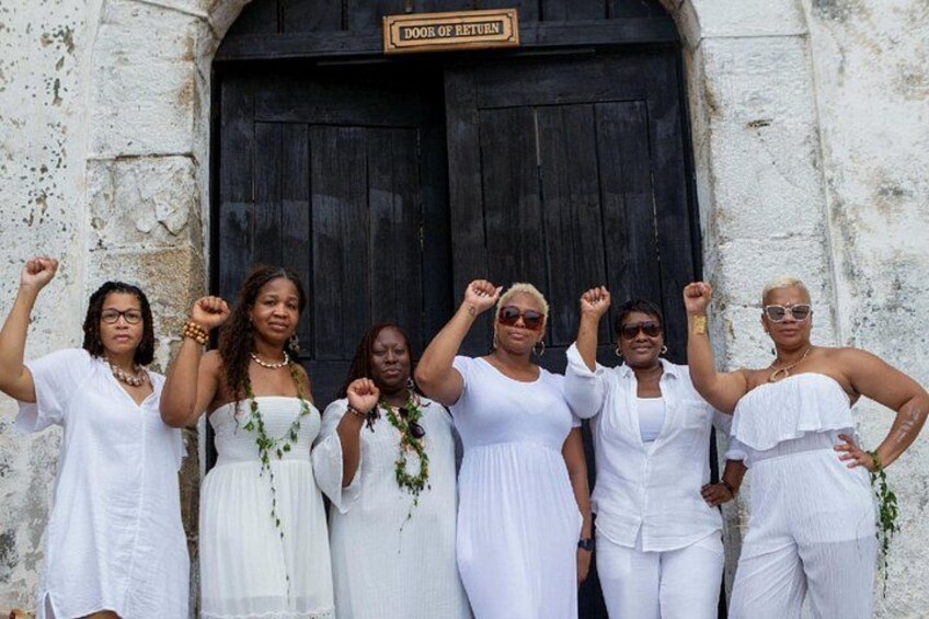 A group of women in white dresses standing in front of a door labeled 'DOOR OF RETURN'. 3