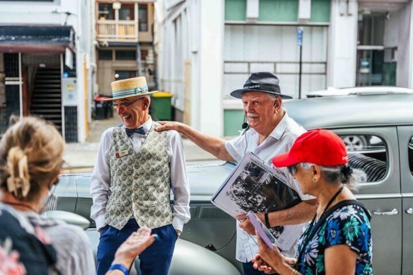 Un grupo de personas de pie junto a un coche antiguo, una sosteniendo un periódico. 5