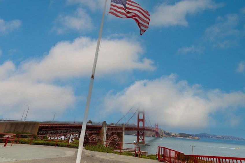 A flagpole with an American flag, a red bridge, and a body of water. 3