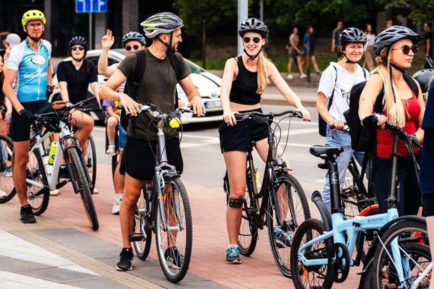 A group of cyclists on a paved path with cars parked on the side. 1