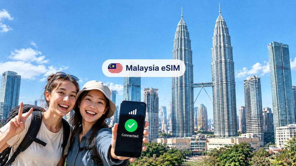 Dos personas tomando un selfie con un teléfono inteligente que muestra el estado 'Connected', frente a las Torres Petronas en Kuala Lumpur. 1