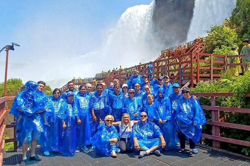 A group of people in blue rain ponchos standing on a bridge with a waterfall in the background. 5