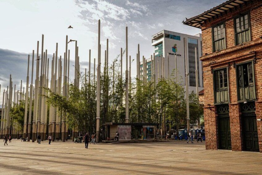 A plaza with tall vertical poles, a modern building labeled 'IMAN PLAZA,' and a traditional brick building. 5