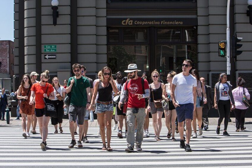 A group of people crossing a street at a crosswalk in front of a building with a sign that reads 'Cfa Cooperativa Financiera'. 2