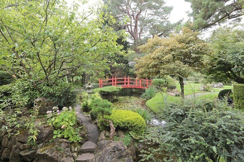 A traditional Japanese garden with a red bridge, stone pathway, and various plants. 2