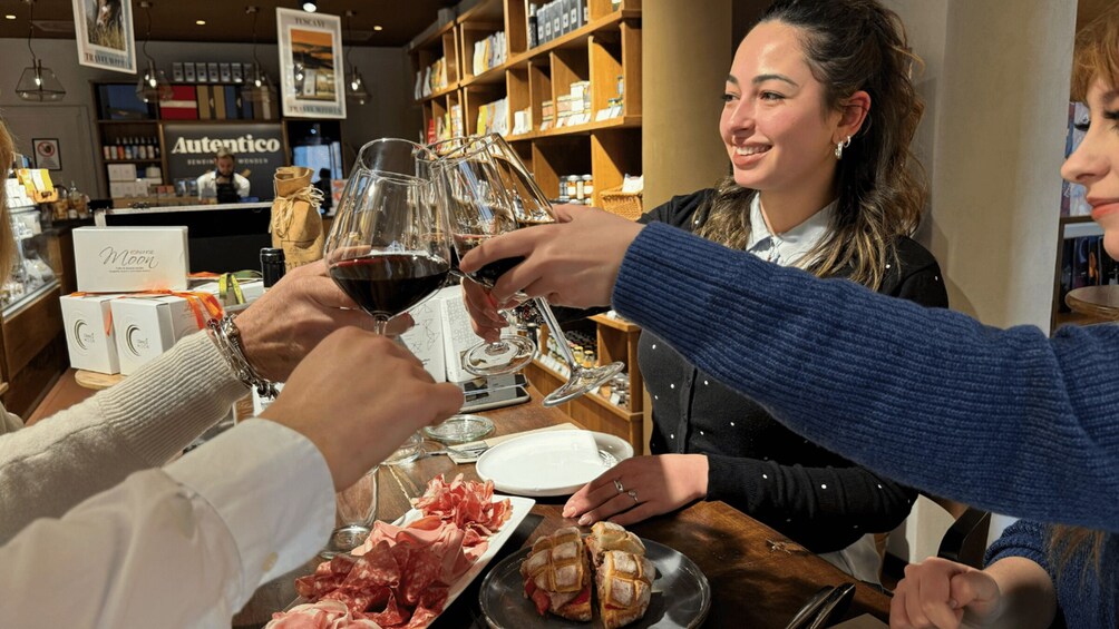 People toasting with wine glasses in a restaurant with shelves of products in the background. 1