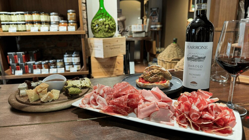 A table with various cheeses, cured meats, a bottle of Barolo wine, and a glass of red wine. 2