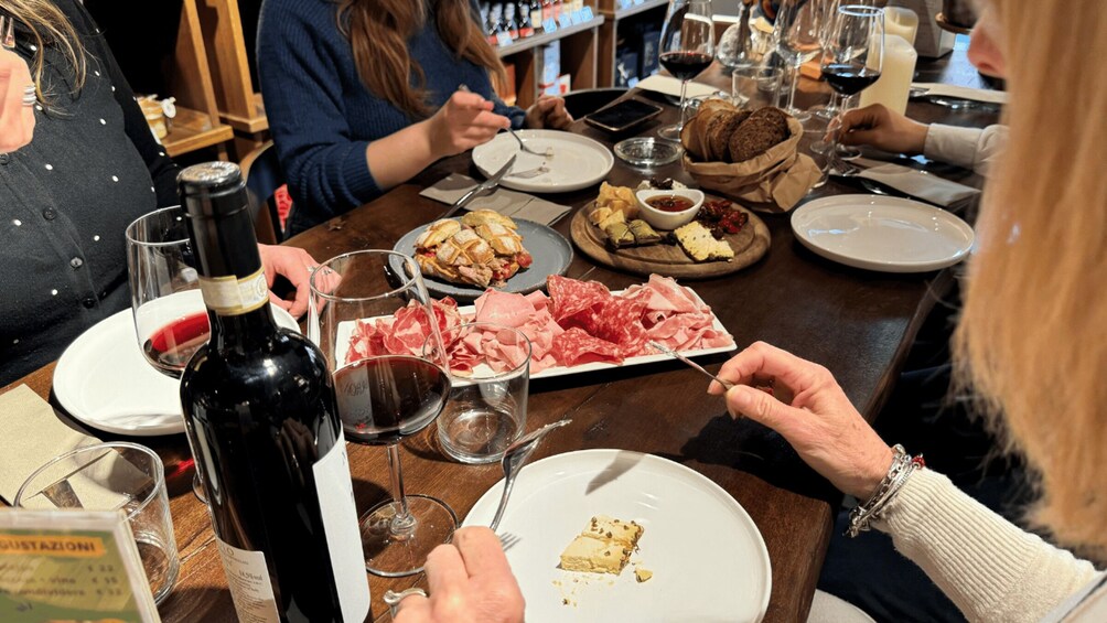 A group of people dining at a restaurant with various dishes, wine glasses, and a bottle of wine on the table. 4