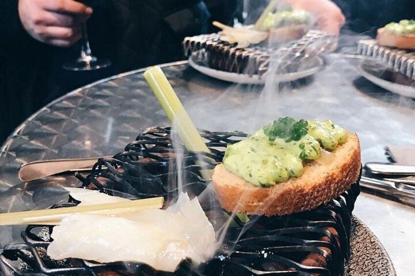 A dining table with a dish of sushi, a piece of sashimi, and a bread with green topping. 3