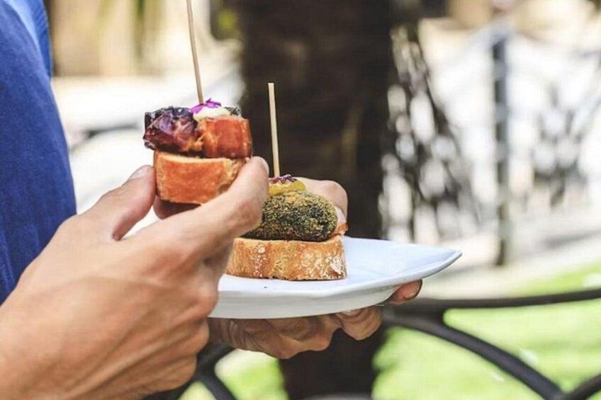 A person holding a white plate with two food items, one with a toothpick. 4