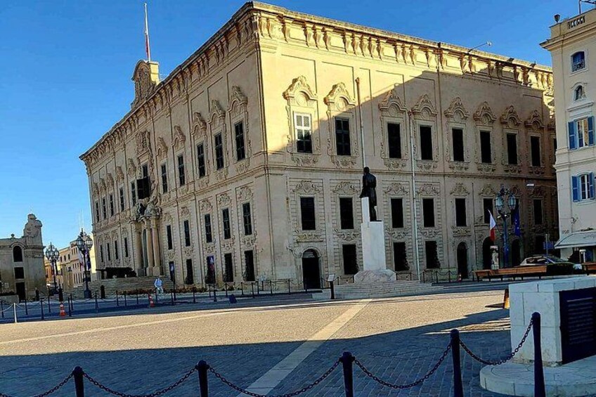 Un edificio histórico con arquitectura clásica, una estatua en primer plano y un cielo azul despejado. 4