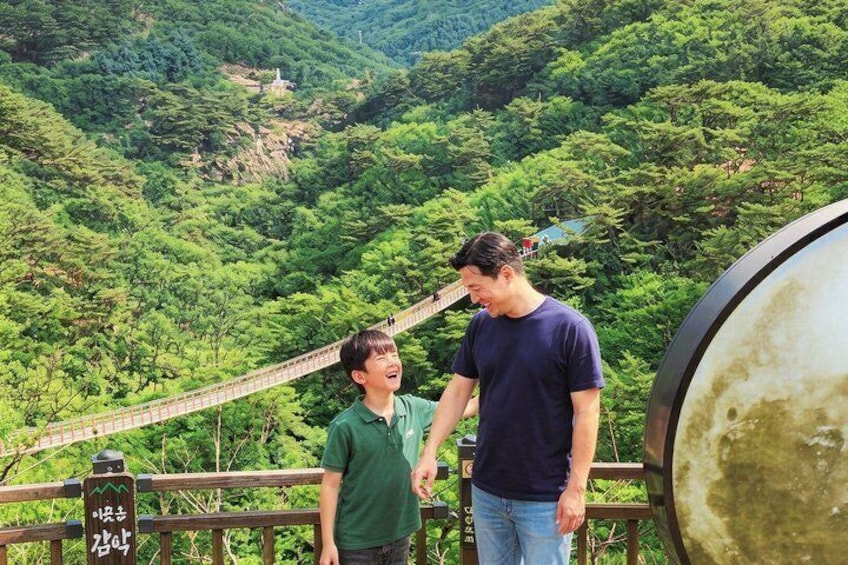 Dos personas sobre un puente con un paisaje montañoso cubierto de bosque. 1