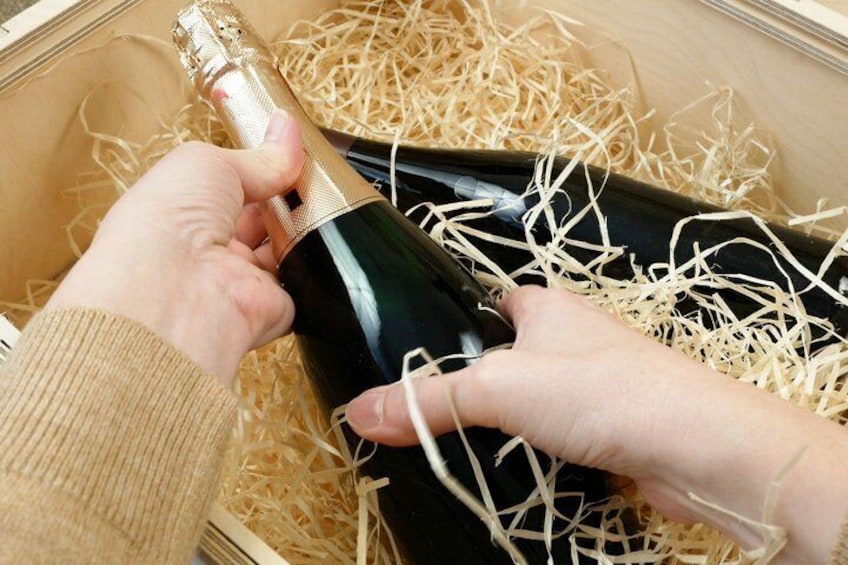 Una persona sosteniendo una botella de champán sobre una caja llena de paja. 3