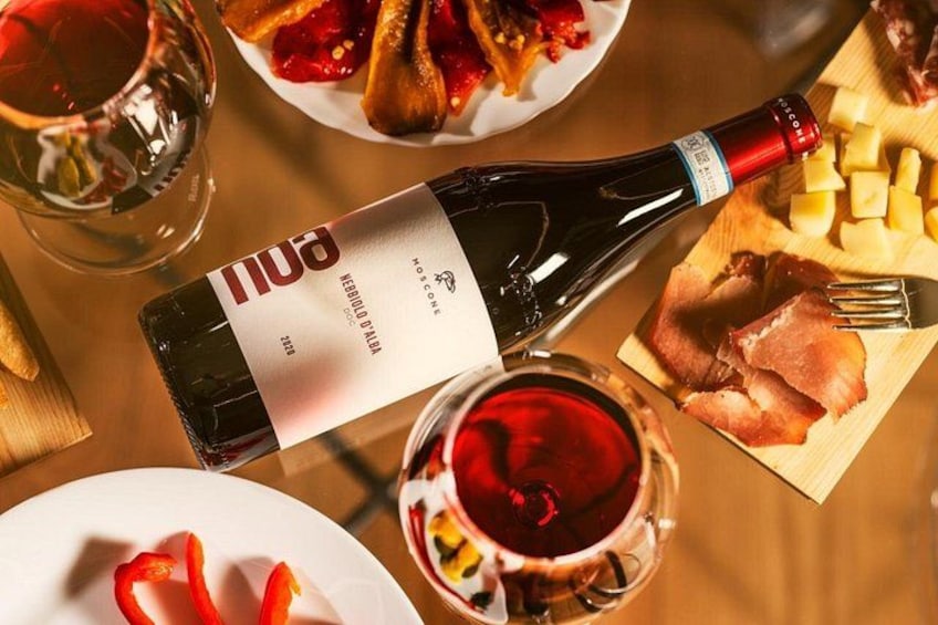 A bottle of red wine, a glass of red wine, a plate with red peppers, and a wooden board with cheese and ham. 1