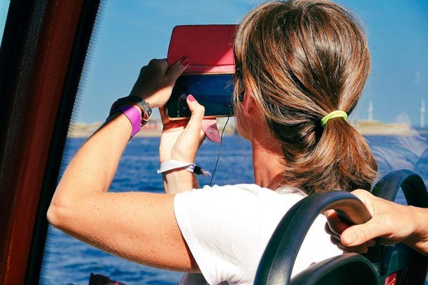 Une personne conduisant un bateau, tenant un appareil rouge, avec un ciel dégagé et de l’eau en arrière-plan. 2