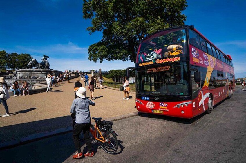 Un autobus a due piani rossi con la scritta 'Copenhagen' sul lato, parcheggiato in una zona pubblica con persone nelle vicinanze. 2