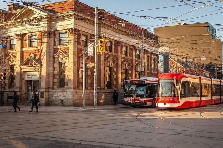A tram station with two trams, a historic building, and a pedestrian crossing. 5