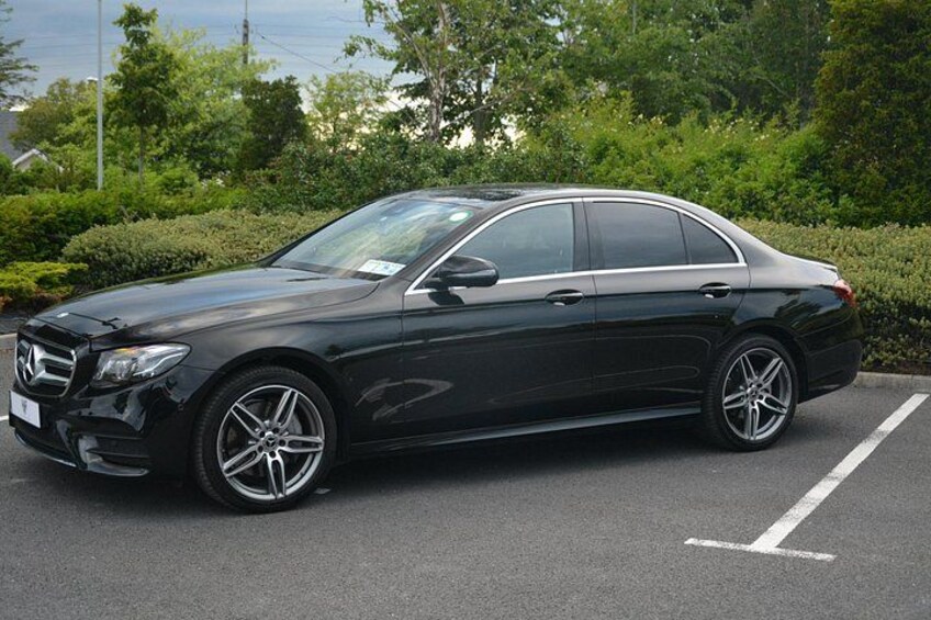 En svart Mercedes-Benz står parkerad på en parkeringsplats med grönska i bakgrunden. 5