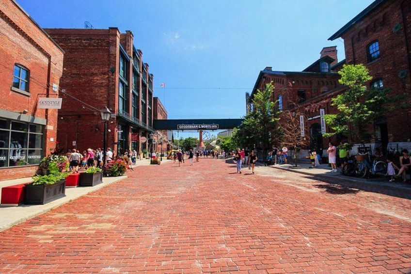 A brick-paved street with buildings, a clear sky, and people walking. 3
