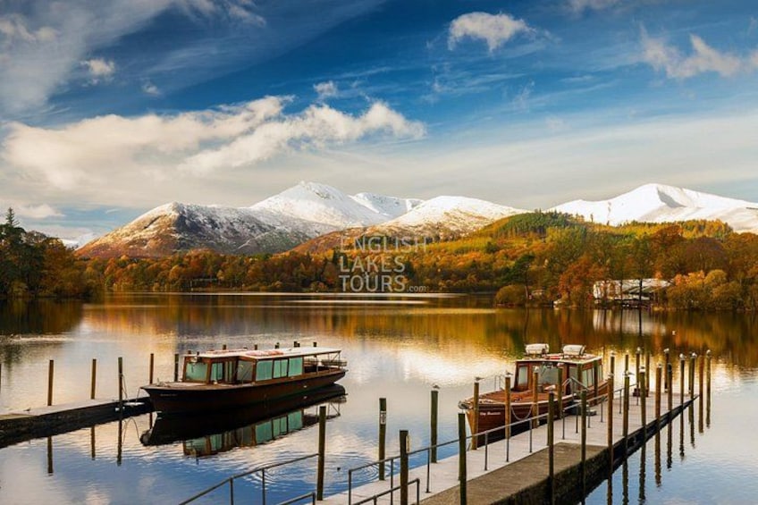 A lake with a boat docked at the pier, surrounded by mountains and autumn foliage. 2