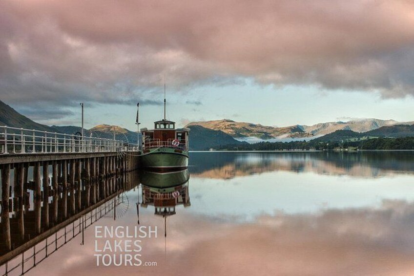 A calm lake with a dock and a boat, surrounded by mountains and a cloudy sky. 5