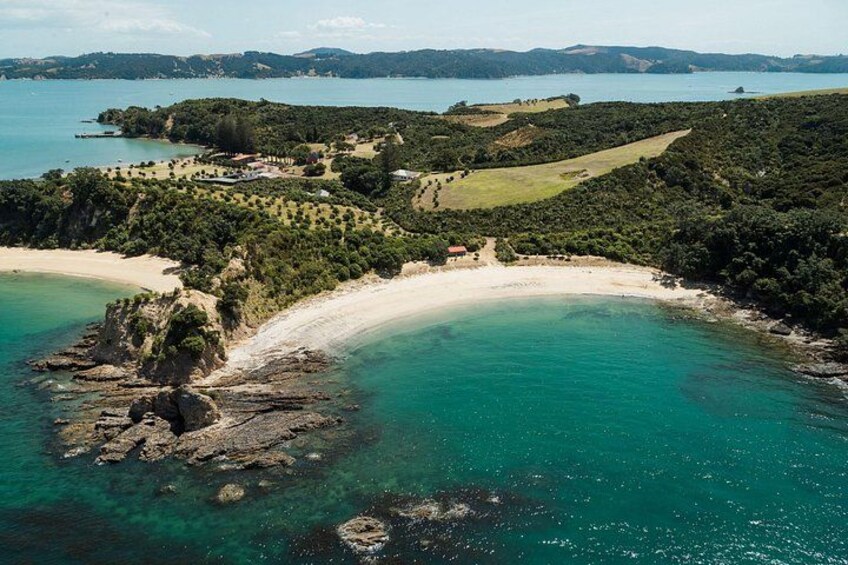 A coastal landscape with a sandy beach, clear turquoise waters, and a forested area with a small building. 2
