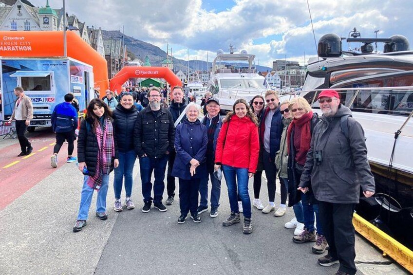 Un grupo de personas frente a un evento de maratón, con un barco y un paisaje urbano al fondo. 3