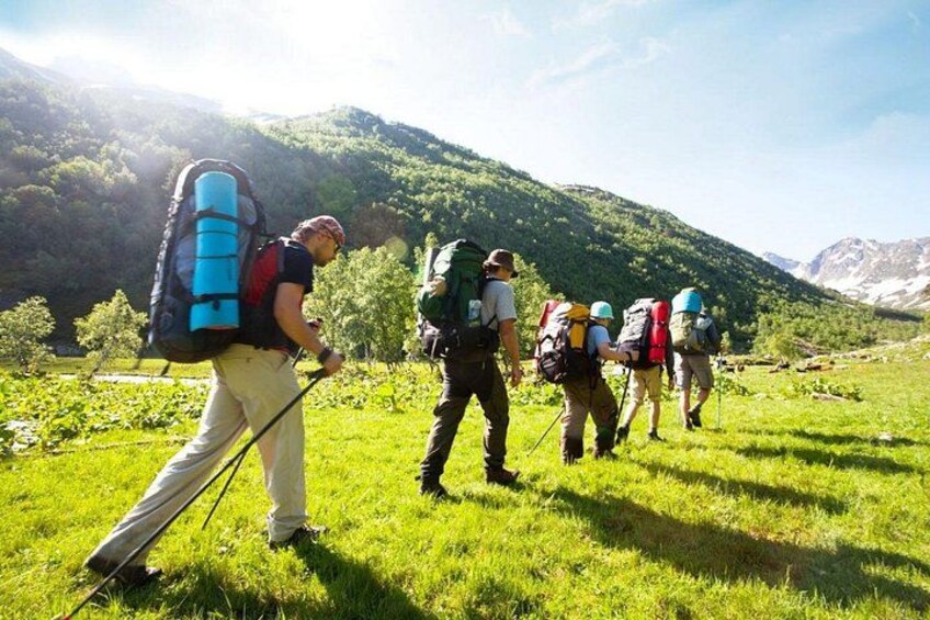 A group of hikers with backpacks in a grassy field with mountains in the background. 1