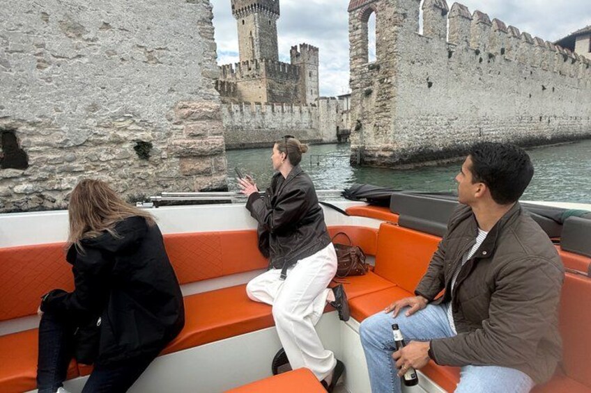 Turister på en båt med en historisk stenmur och ett slott i bakgrunden. 2