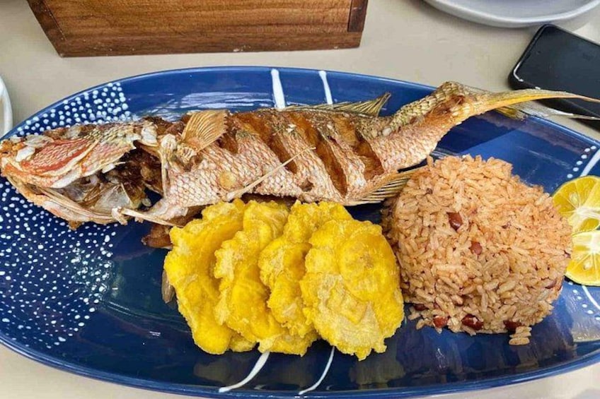 A plate with fried fish, yellow plantains, and rice. 2