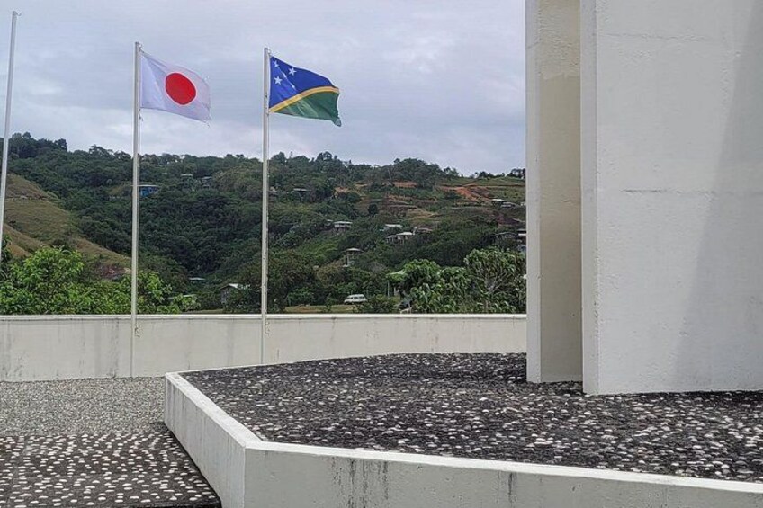 Deux drapeaux flottant au sommet de mâts, une structure en béton et, au loin, un paysage vallonné. 3