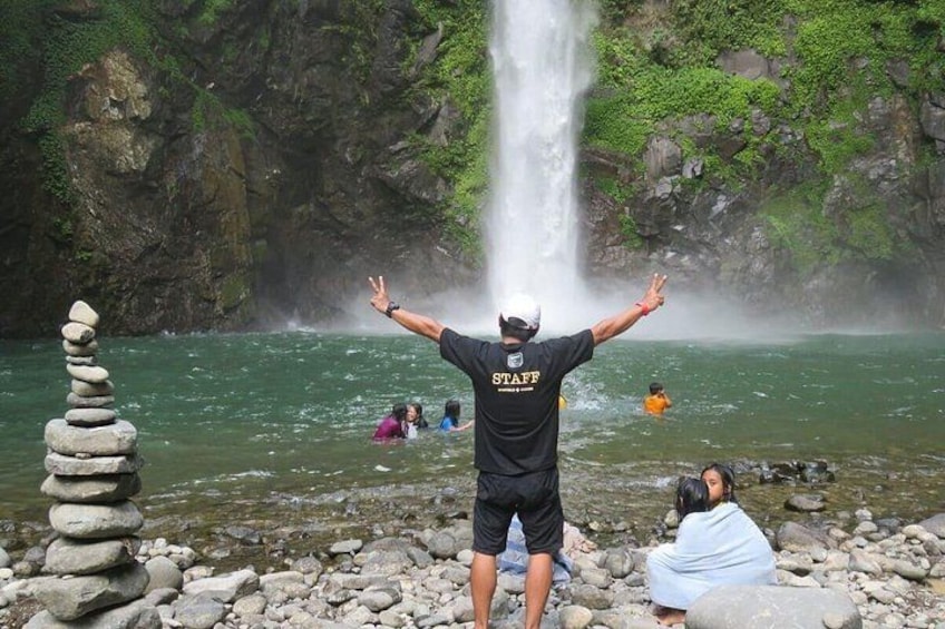 Una persona in piedi con le braccia aperte di fronte a una cascata, circondata da rocce e vegetazione. 2
