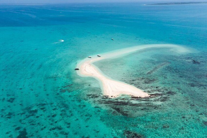 An aerial view of a turquoise sea with a sandy beach curving into the water, surrounded by coral reefs. 1