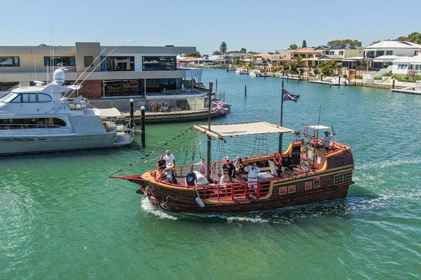 A wooden boat with passengers, docked at a marina with other boats and buildings in the background. 5
