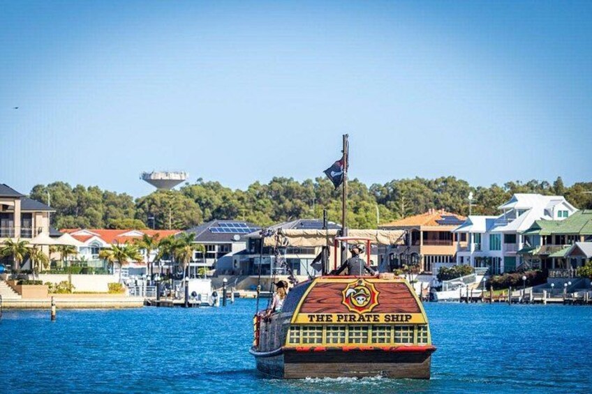 A boat named 'The Pirate Ship' with a flag, docked at a waterfront with houses and a hill in the background. 2