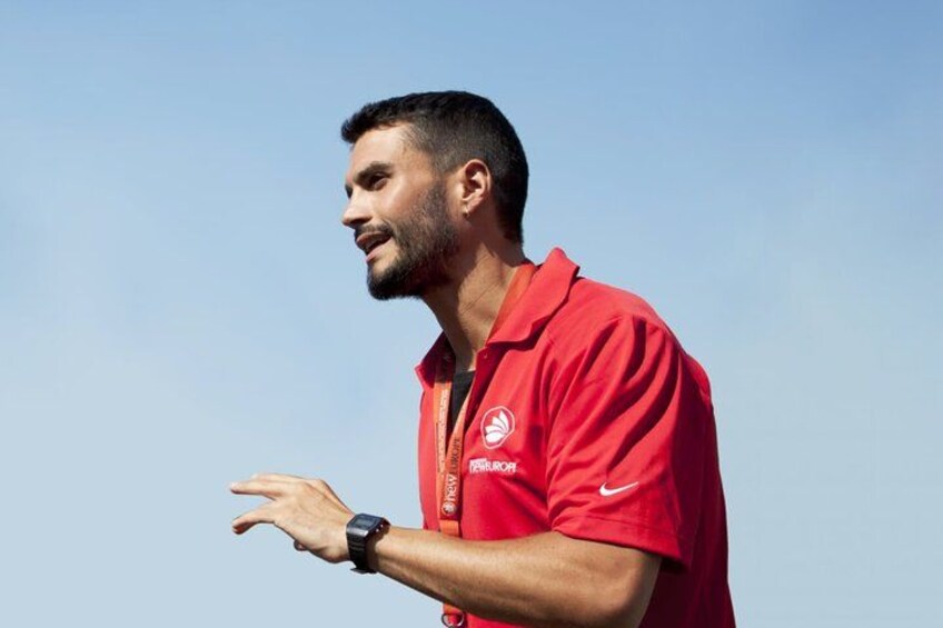A person wearing a red shirt with a logo, standing outdoors with a clear sky in the background. 1