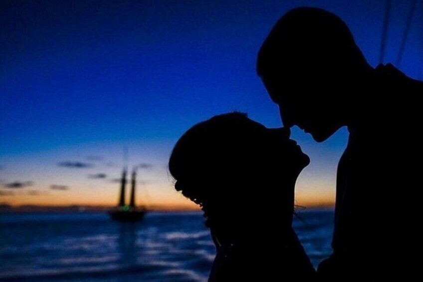 La silhouette d’un couple se découpant sur le ciel d’un coucher de soleil, avec un navire en arrière-plan. 4
