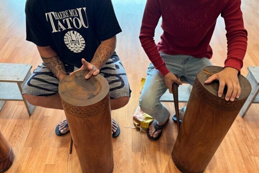 Two people sitting on chairs, each holding a wooden drum. 3