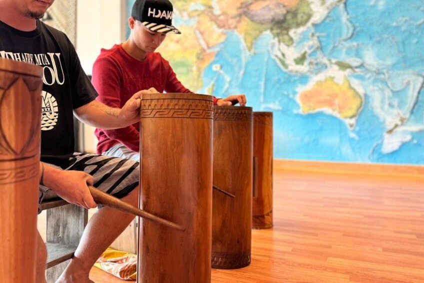 Two individuals playing wooden percussion instruments in a room with a world map on the wall. 1