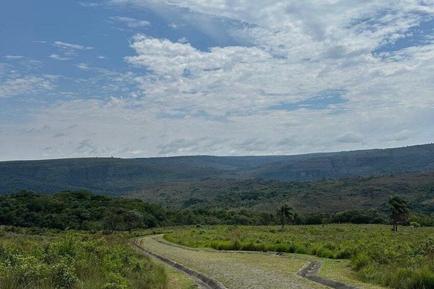 A winding dirt road through a grassy landscape with distant hills under a partly cloudy sky. 4