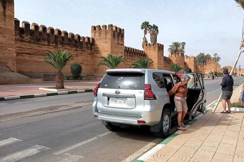Ein silberner SUV parkt auf einer Straße, im Hintergrund eine große, historische Steinmauer. 1